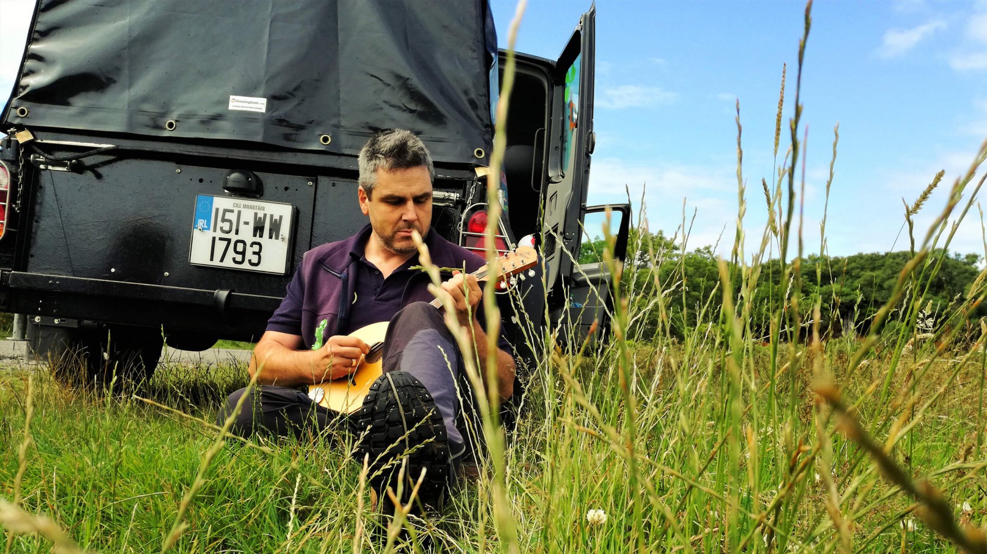 VagaGuide Tour Guide Tim playing his mandolin on tour beside his Vagabond tour vehicle in Ireland