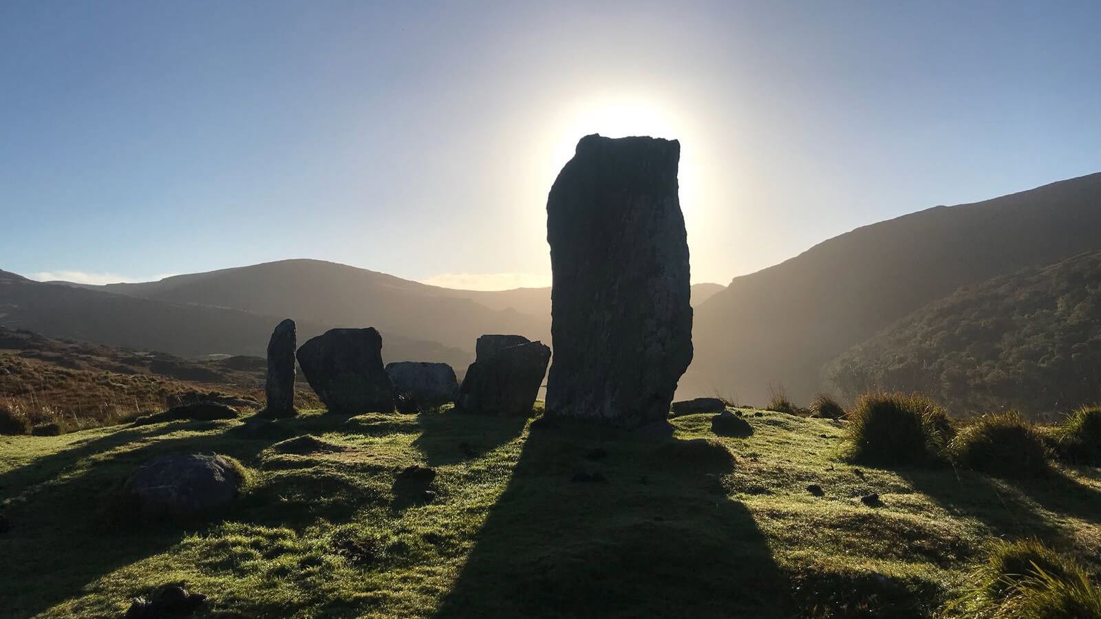A silhouette of the Uragh stone circle as the sun beams behind it 