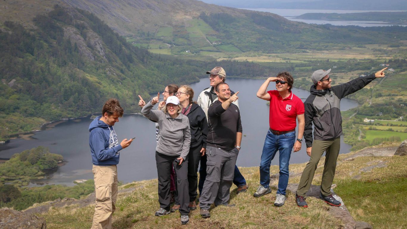 A group of Vagabond tour guests smile and point in different directions at Ladies View in Ireland