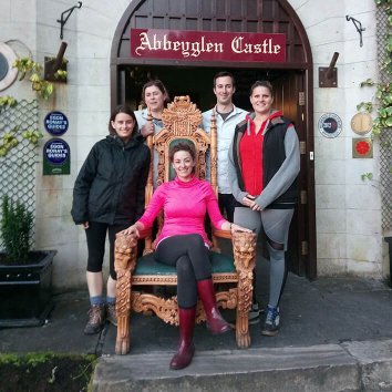 Family posing for a picture with woman sitting on the throne in front of Abbeyglen Castle Family posing for a picture with woman sitting on the throne in front of Abbeyglen Castle