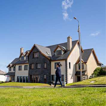 The exterior of waterfront house in the sun with a lady walking past