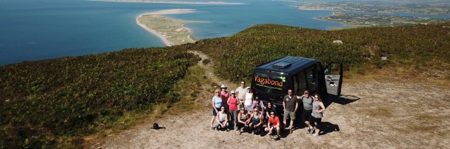 Vagabond Tour Group posing beside VagaTron 4x4 tour vehicle at a scenic mountain site in Ireland