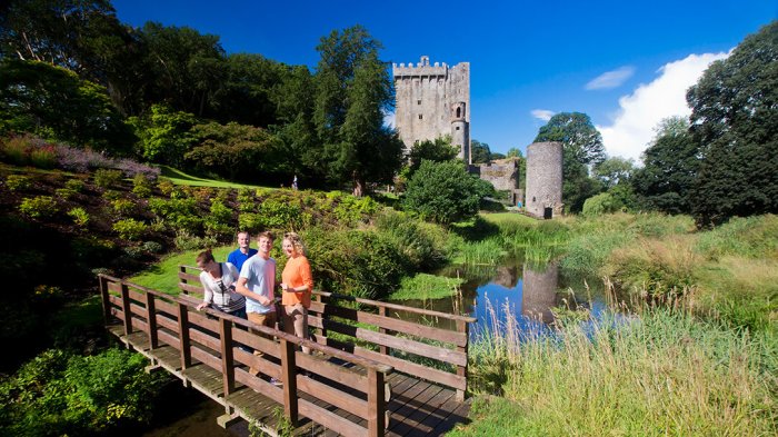 Discover the rich history and enchanting charm of Blarney Castle Two women and two men crossing the bridge in Blarney Gardens with Blarney Castle in the background