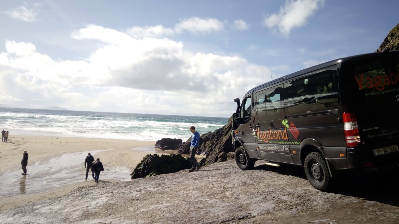 A Vagatron tour vehicle drives onto a beach in Ireland with guests in the background
