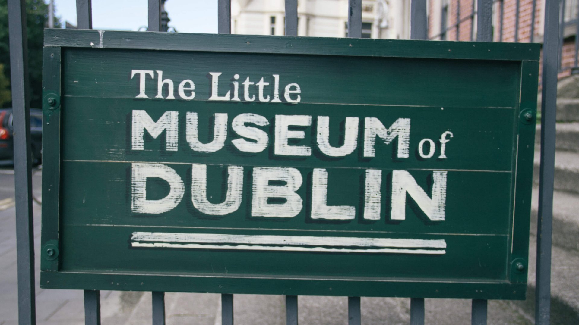 Green sign for Little Museum of Dublin hangs on a railing